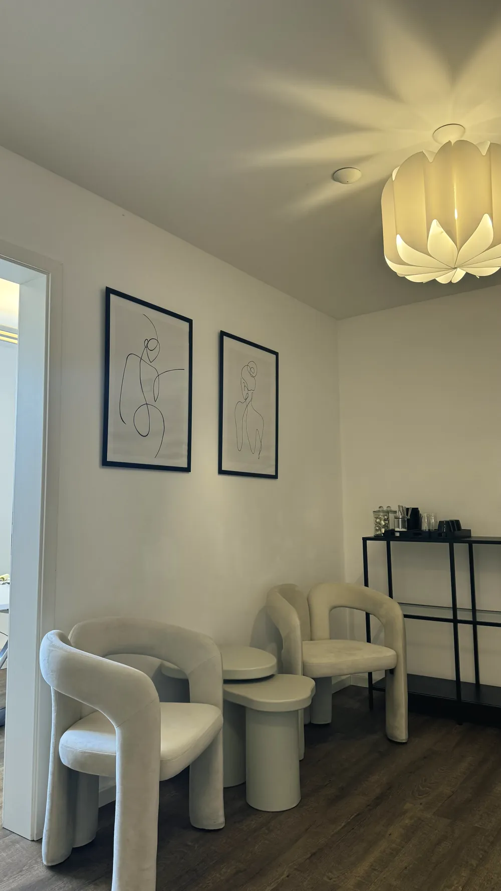 Wartebereich mit zwei hellen Sesseln, Line-Art-Bildern und einer warm leuchtenden Deckenlampe